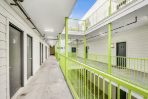 Outdoor hallways to apartment units, lime green railing, photo taken from 3rd story, emergency exit at end of hallway.